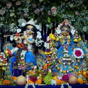 Intricate Krishna and Radha statues adorned with flowers and ornaments, set in vibrant decor.