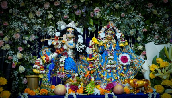 Intricate Krishna and Radha statues adorned with flowers and ornaments, set in vibrant decor.